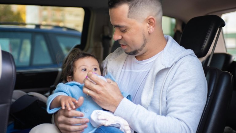A parent's hand using a portable travel formula dispenser to quickly prepare a baby bottle, illustrating convenient and hygienic feeding for infants on the go during travel.