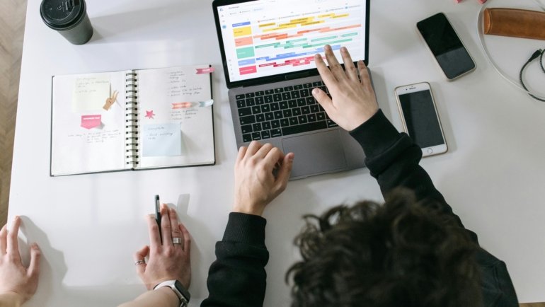 Hands writing travel company name ideas in a notebook with a pen, surrounded by a world map and a compass, symbolizing the creative process of branding a new travel business.