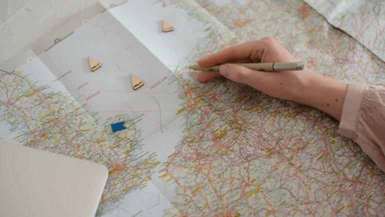 Traveler's hands open on a 'Norway travel guide book' with a map, planning an exciting 2025 adventure to Norwegian fjords and cities, highlighting detailed preparation.