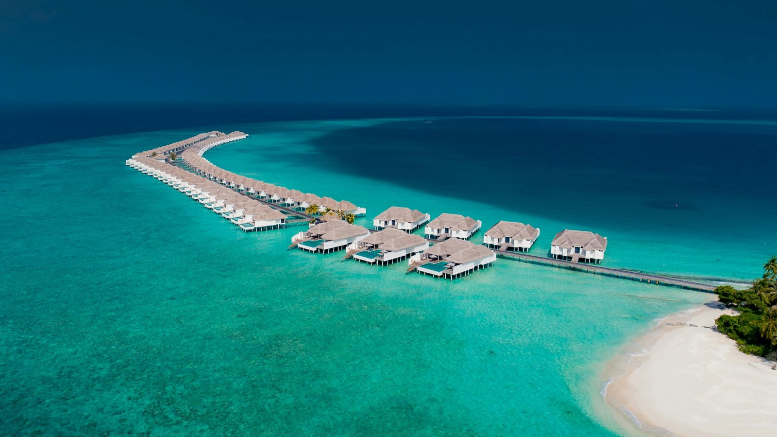 Maldives luxury overwater villa with a private deck over sparkling turquoise water and a pristine white-sand beach, ideal for all-inclusive travel packages and romantic island escapes.