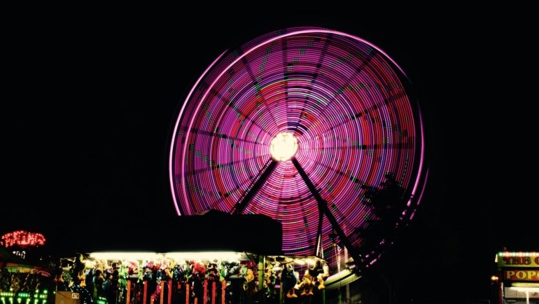 Vibrant traveling carnival at night with illuminated rides such as a Ferris wheel, a bustling crowd, and colorful lights, representing the excitement of mobile amusement parks and community fairs.