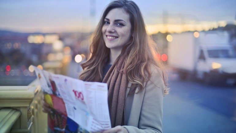 Smiling Licensed Practical Nurse (LPN) with a travel bag, looking confidently at a vibrant city skyline, representing rewarding travel nursing career opportunities and personal adventure.