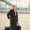 A modern traveler effortlessly navigates a bustling airport terminal, with a stylish personal item bag securely attached to a rolling carry-on suitcase using a smart trolley sleeve, demonstrating hands-free convenience.