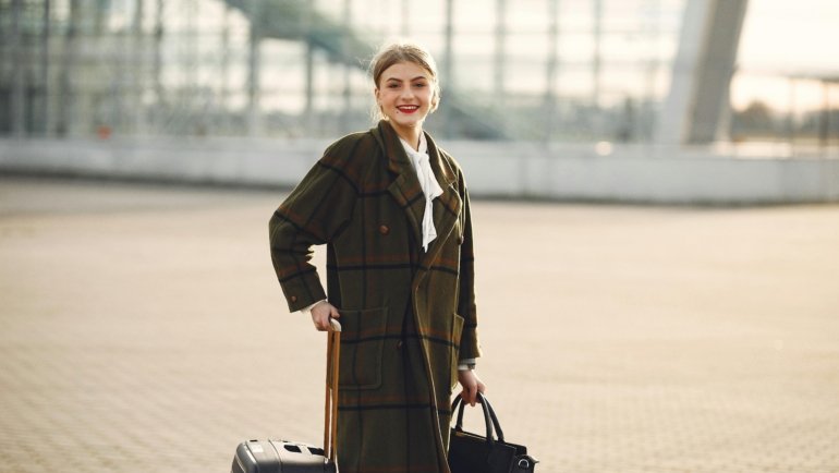 A modern traveler effortlessly navigates a bustling airport terminal, with a stylish personal item bag securely attached to a rolling carry-on suitcase using a smart trolley sleeve, demonstrating hands-free convenience.