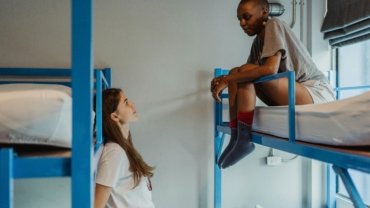 Diverse travelers engaging in lively conversation in a comfortable common area of a modern travellers inn, highlighting community and affordable accommodation for backpackers.