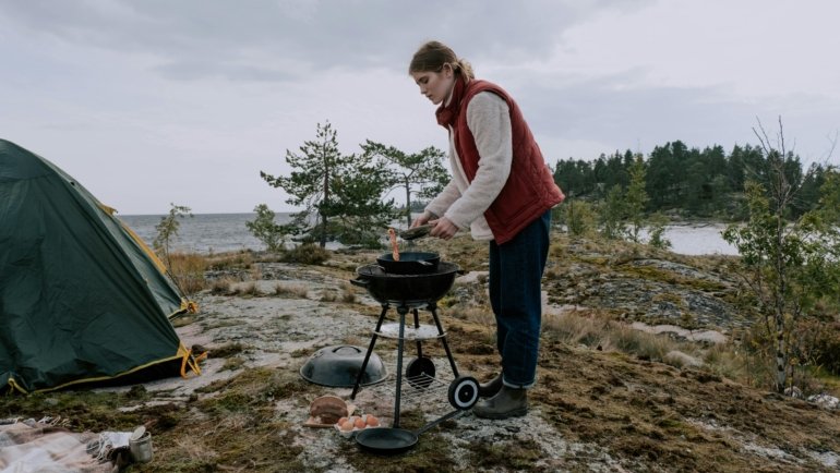 Portable traveller grill cooking delicious food for happy campers in a scenic outdoor setting, ideal for camping and adventure.