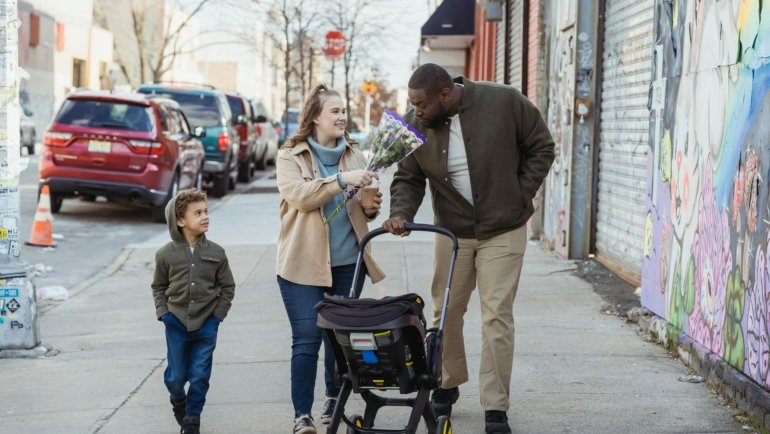 Modern parents effortlessly pushing a Babyzen YOYO² compact travel pram with their baby through a busy airport terminal, symbolizing stress-free family travel and urban adventures with a lightweight, easy-fold stroller.