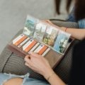 Close-up of hands turning pages of a physical travel photo album, filled with curated memories and photos from past adventures, highlighting the tangible joy of storytelling.