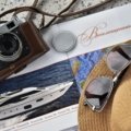 Luxury travel accessories including designer luggage, silk travel pillow, noise-cancelling headphones, and RFID-blocking wallet arranged in a stylish flat lay