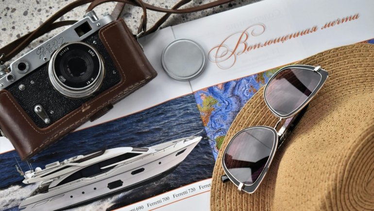 Luxury travel accessories including designer luggage, silk travel pillow, noise-cancelling headphones, and RFID-blocking wallet arranged in a stylish flat lay