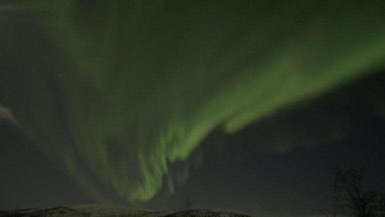 Northern Lights over snowy Finnish landscape in winter with forests and mountains