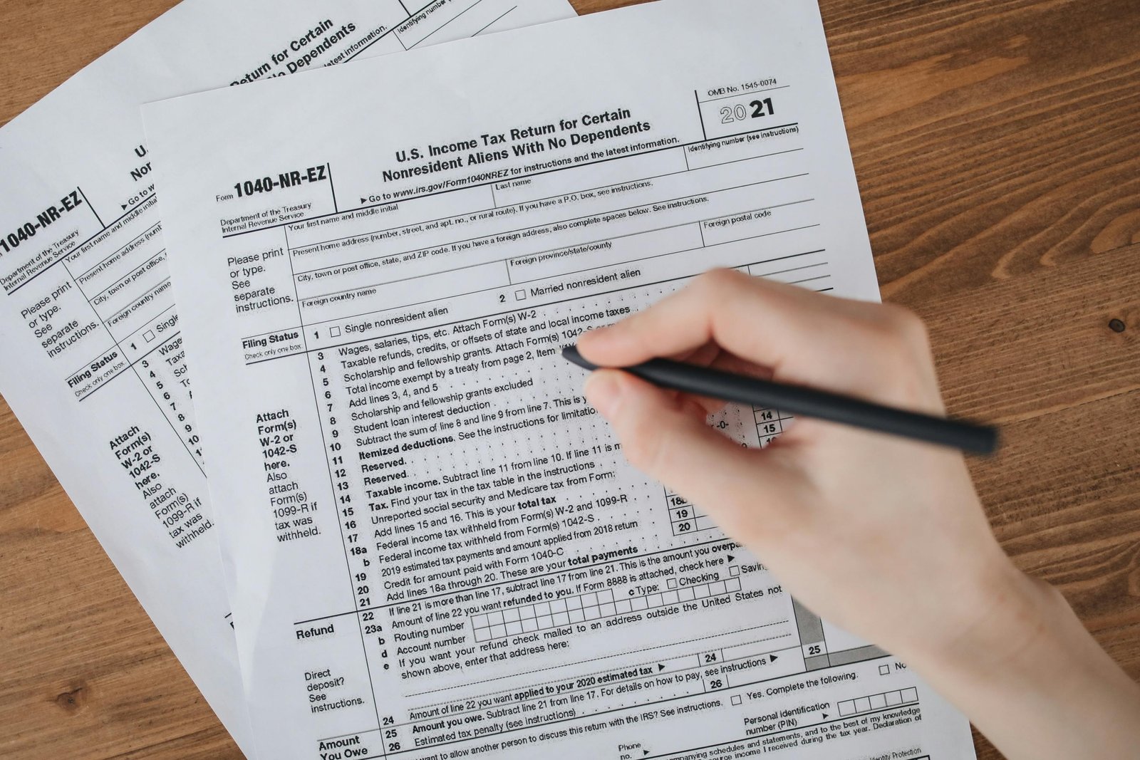 Person filling out USCIS N400 naturalization form with travel documents and passport on desk