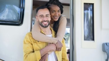 Couple relaxing outside a compact travel trailer during a camping trip in nature
