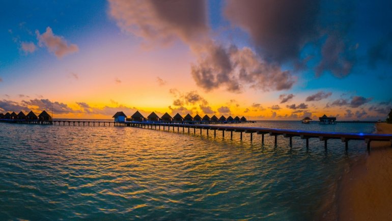 Stunning tropical beach at sunset with clear lagoon and luxurious overwater bungalows in an exotic travel destination