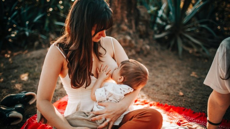 Mother breastfeeding baby using a compact travel breastfeeding pillow outdoors for comfort and support