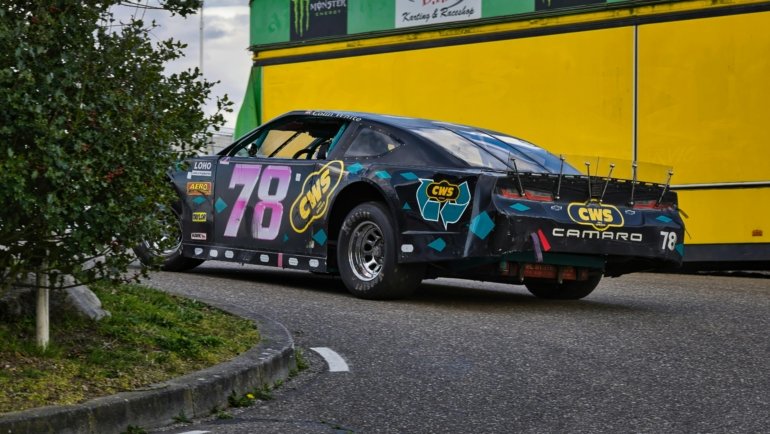 Traveler whiskey glass with rich amber whiskey next to fast NASCAR racing action, representing the fusion of premium whiskey and motorsport culture
