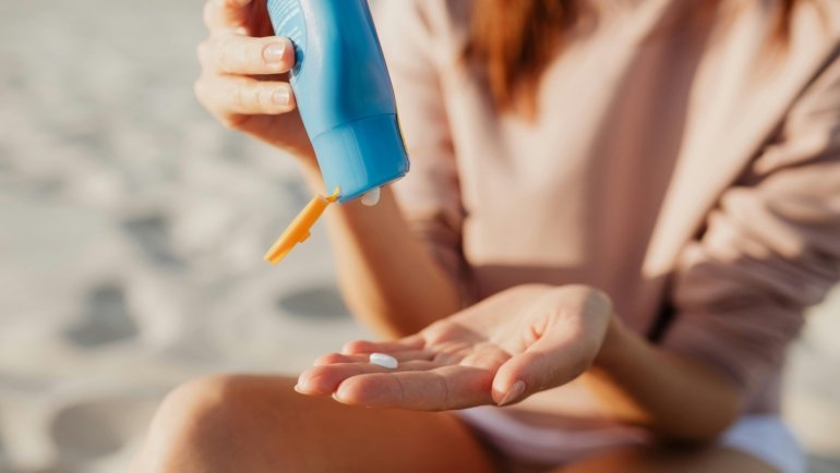 Traveler applying travel-size sunscreen lotion on skin outdoors at the beach for sun protection and skin care