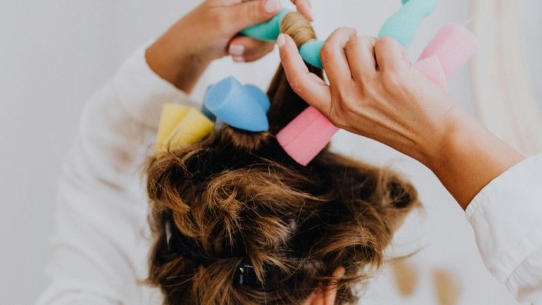 Woman styling hair with travel hair curlers rollers in a hotel room, showcasing lightweight portable hair styling tools for travelers