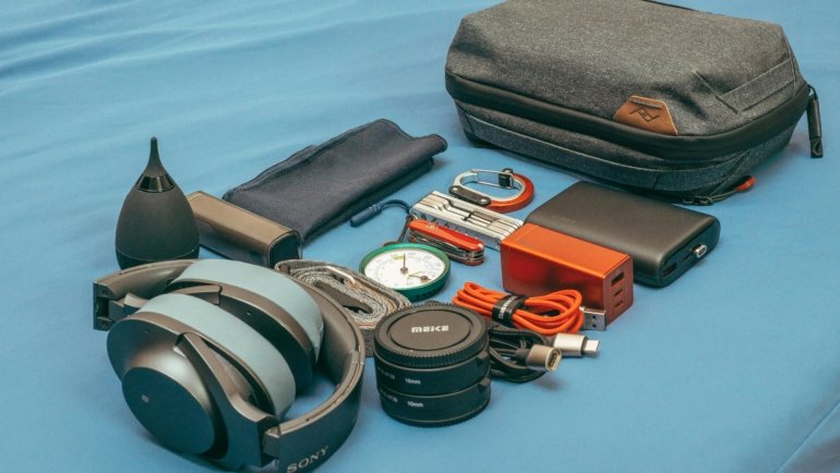 Flat lay of travel gifts including neck pillow, packing cubes, portable charger, scratch-off map, and personalized luggage tags