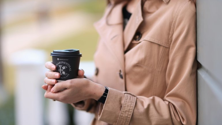 Personalized travel coffee cup held outdoors by traveler, reusable and eco-friendly beverage container