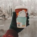 Christmas themed travel coffee mug with festive design held outdoors in winter