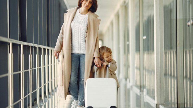 Parent wheeling a child's car seat on a travel cart through an airport for easy family travel