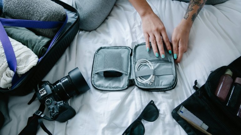 Woman packing travel accessories including organizer bags, compression cubes, and crossbody bag for a comfortable and stylish trip