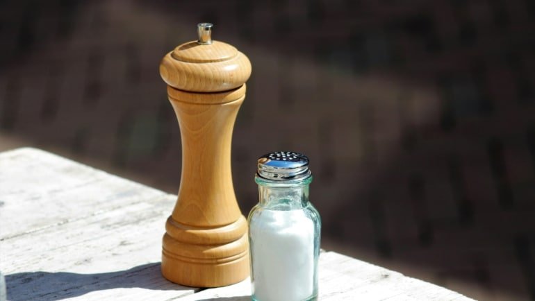 Compact travel salt and pepper shakers used outdoors during a camping meal for easy seasoning on the go