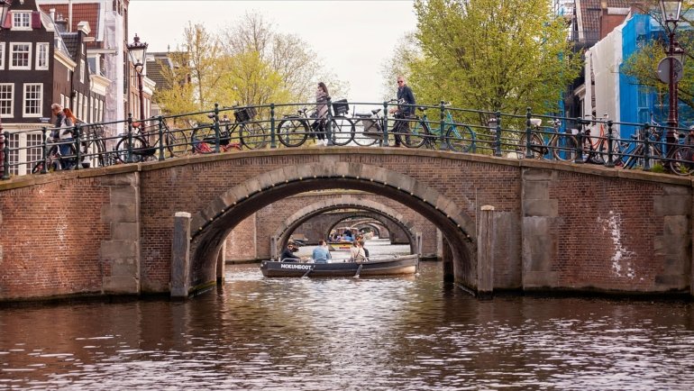 Travelers biking along Amsterdam canals enjoying personalized Netherlands tour and local cultural experience