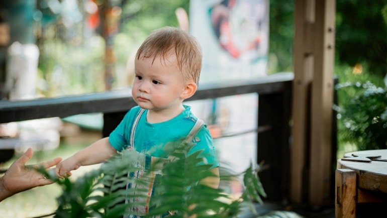 Toddler playing safely in a portable travel playpen outdoors during family trip