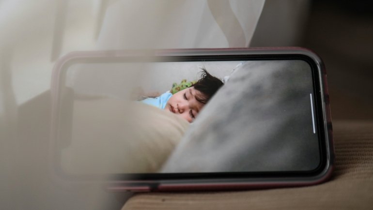 Parent using portable travel baby monitor to safely watch sleeping baby during a trip