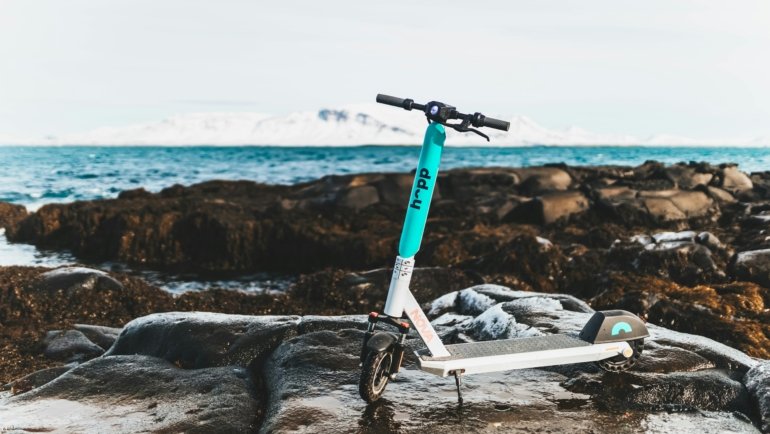 Foldable travel scooter folded and ready to carry in a bright outdoor travel environment