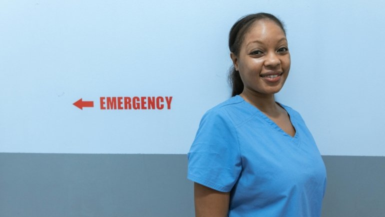Smiling travel nurse with suitcase outside hospital representing American Mobile travel nursing flexibility and opportunities