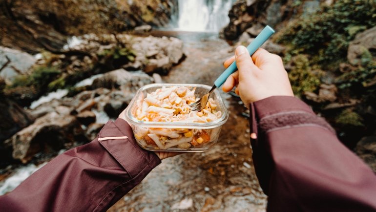 Traveler enjoying a hot meal from a portable food warmer outdoors during a trip