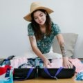 Woman packing travel essentials including clothes, personal care products, and safety tools for a safe and stylish trip