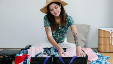 Woman packing travel essentials including clothes, personal care products, and safety tools for a safe and stylish trip