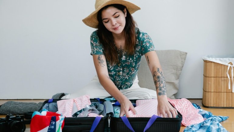 Woman packing travel essentials including clothes, personal care products, and safety tools for a safe and stylish trip