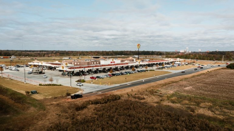 Wide view of a clean and busy highway travel plaza with fuel stations and dining options for travelers