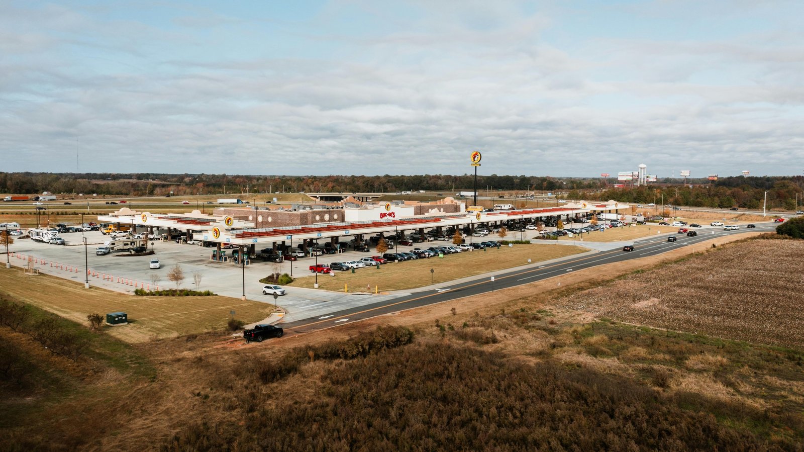 Wide view of a clean and busy highway travel plaza with fuel stations and dining options for travelers
