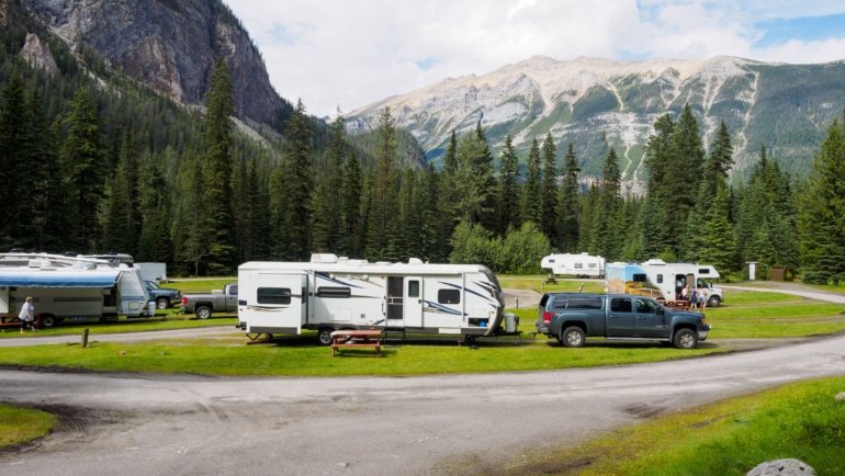 Lightweight rpod travel trailer parked at a picturesque campsite with mountains and forest background