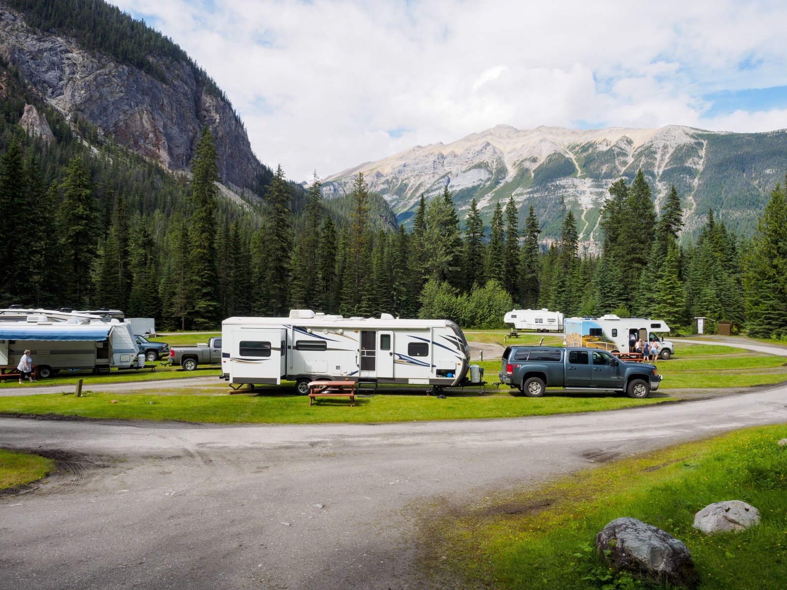 Lightweight rpod travel trailer parked at a picturesque campsite with mountains and forest background