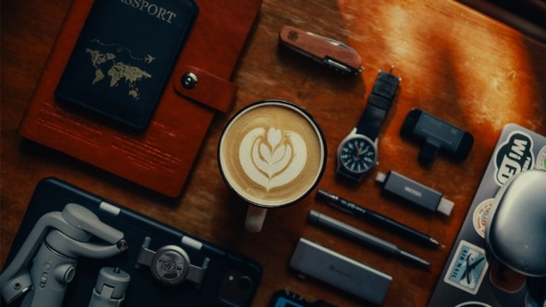Flat lay of essential travel gadgets and accessories including portable charger, travel pillow, noise-cancelling headphones, and travel journal