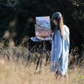Artist painting outdoors with a portable travel easel in a natural scenic environment
