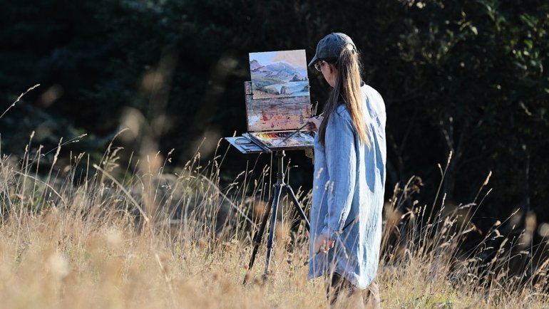 Artist painting outdoors with a portable travel easel in a natural scenic environment