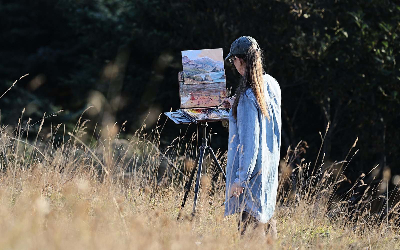Artist painting outdoors with a portable travel easel in a natural scenic environment
