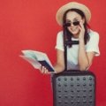 Smiling traveler holding round-trip plane ticket with luggage at airport, representing convenient and affordable travel planning