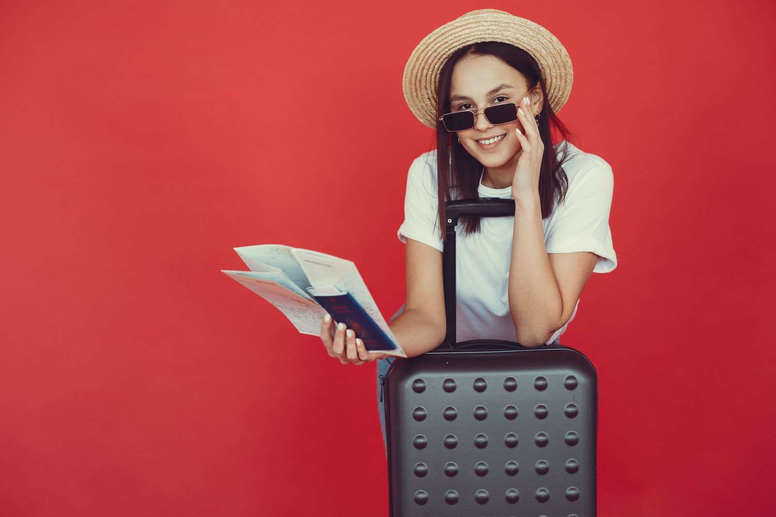 Smiling traveler holding round-trip plane ticket with luggage at airport, representing convenient and affordable travel planning