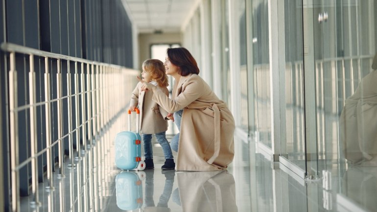 Parent carrying child booster seat in protective travel bag with wheels in airport terminal
