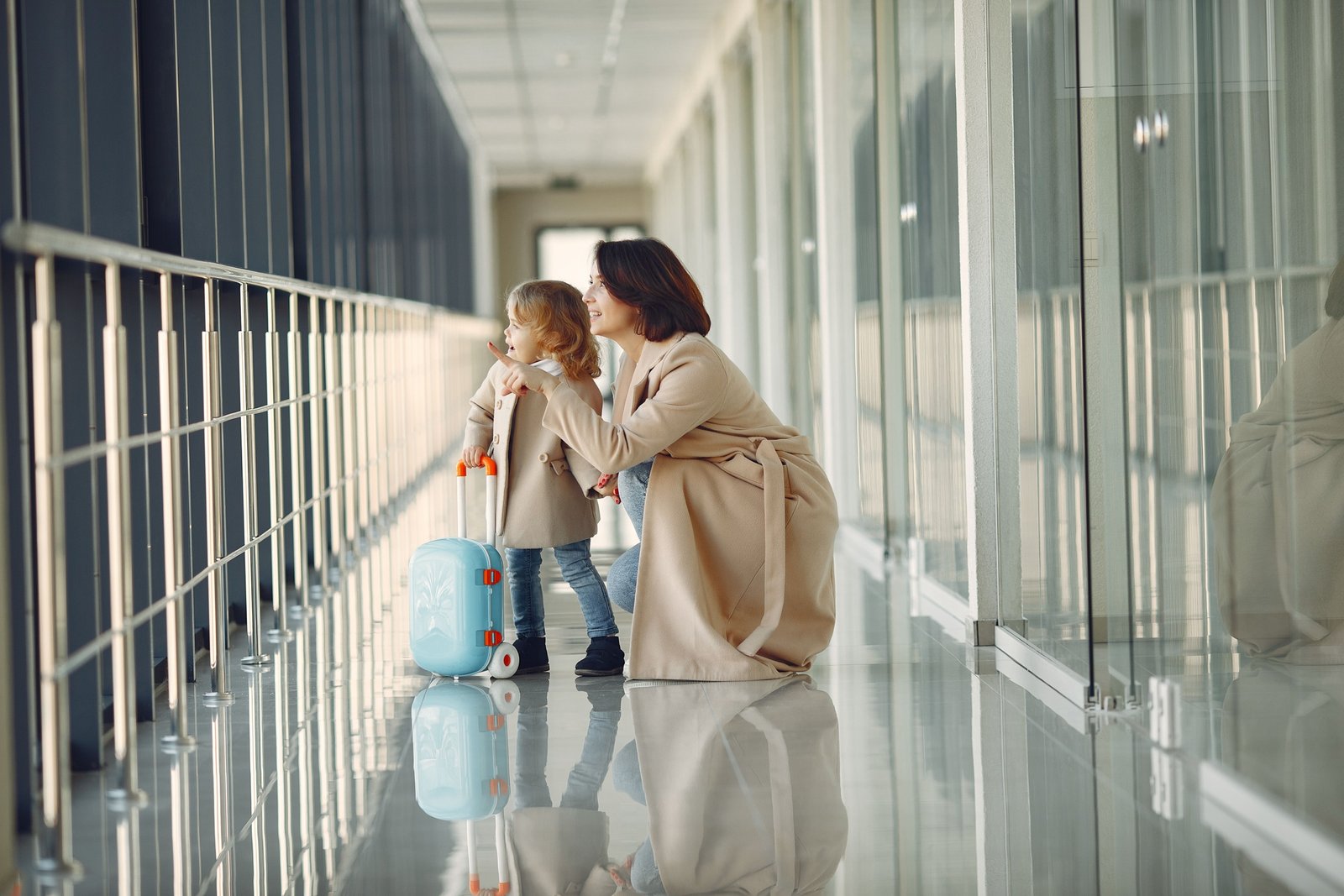 Parent carrying child booster seat in protective travel bag with wheels in airport terminal