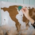 Hand scratching a colorful scratch off travel map showing visited countries and travel adventure